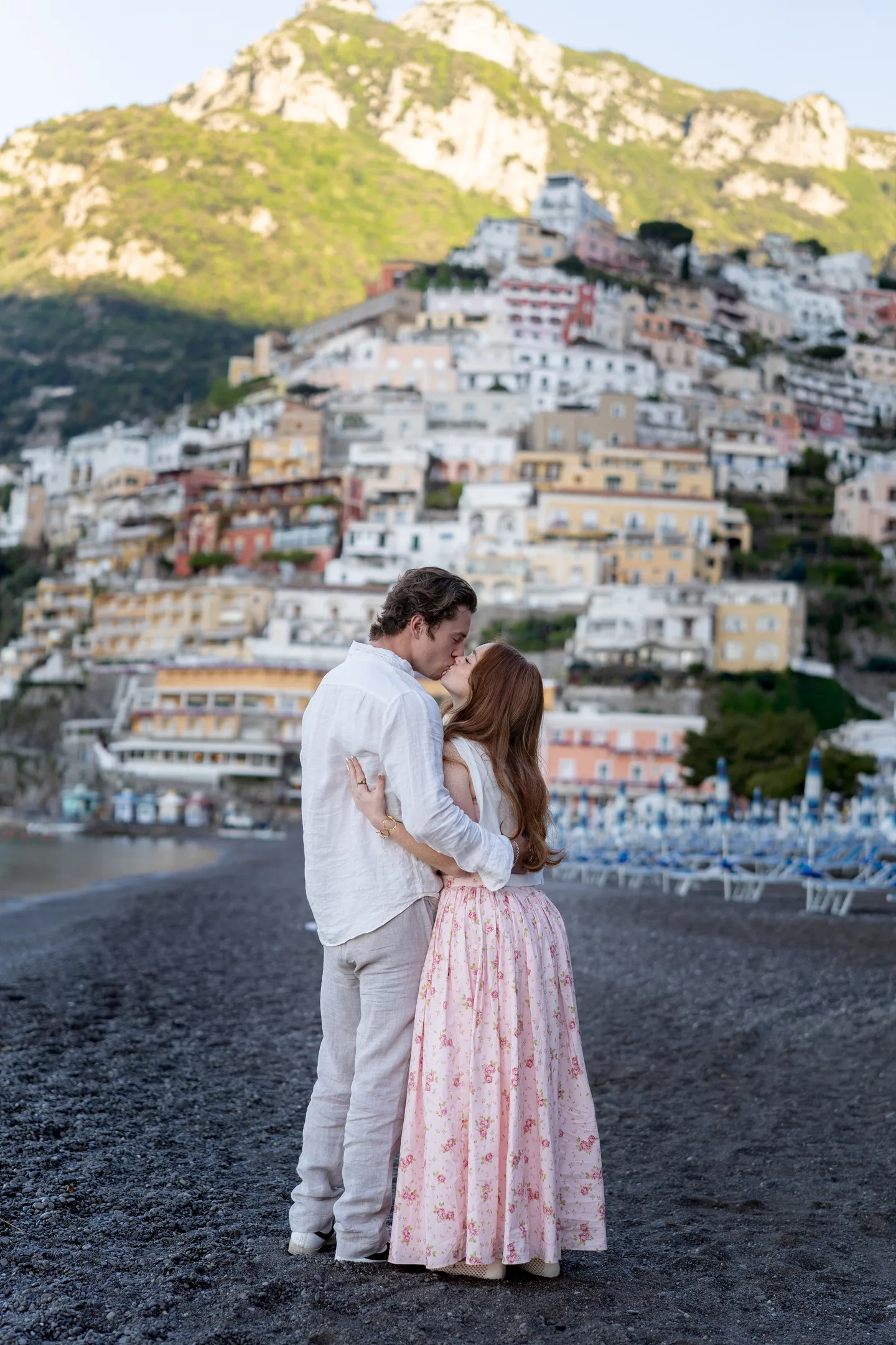 The couple embracing with Positano rising behind them
