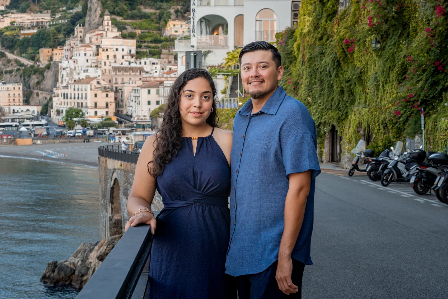 The couple beside the railing with Amalfi’s hillside behind them
