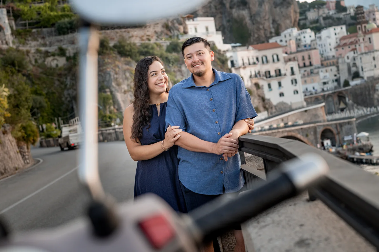 The couple smiling in a scooter mirror with Atrani behind them
