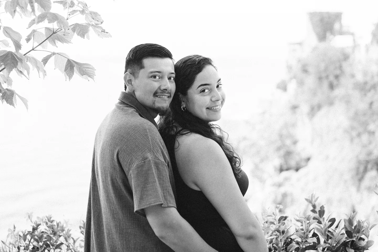 A black-and-white portrait of the couple beneath leafy branches