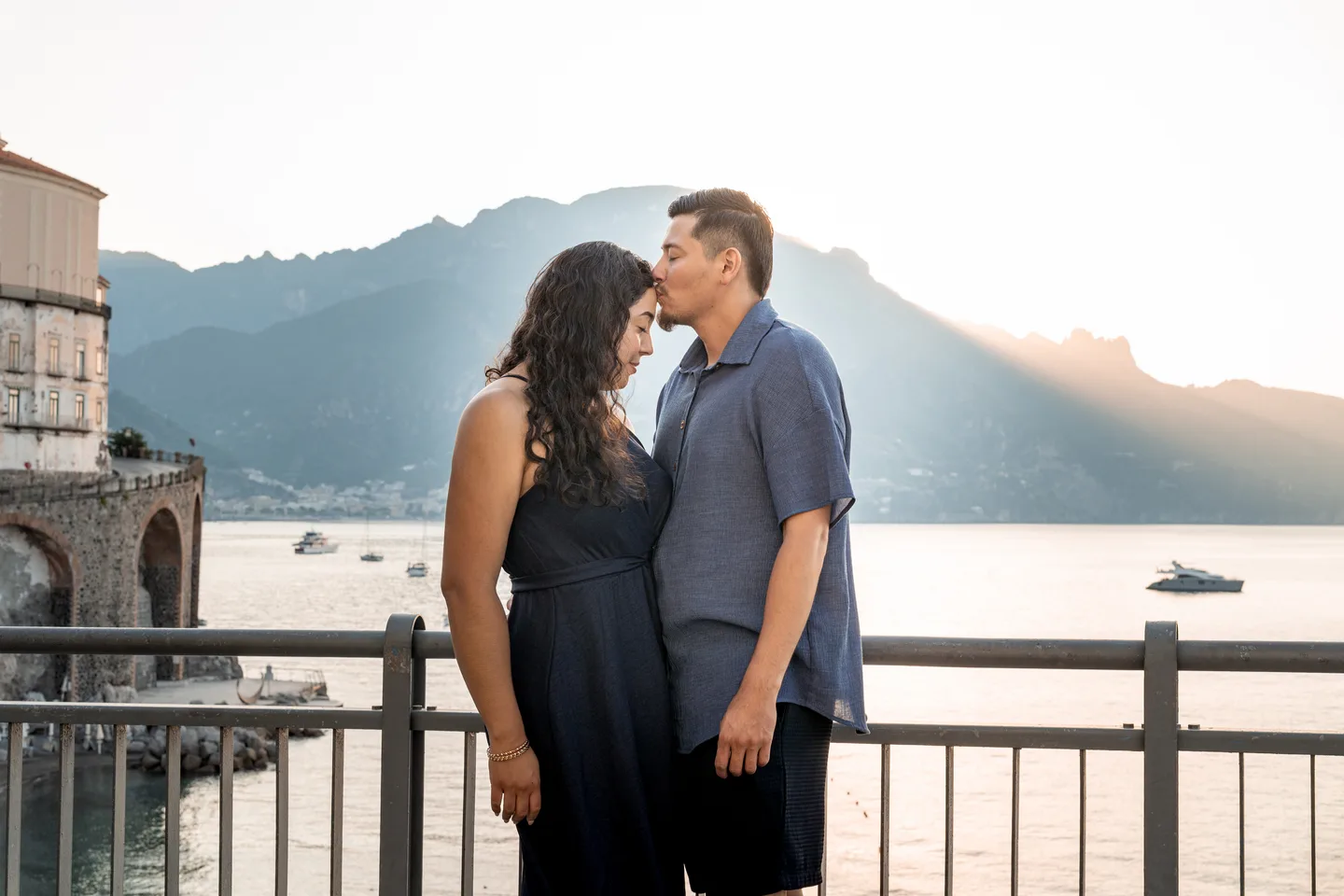 The couple leaning towards a kiss as the sun rises over the mountains