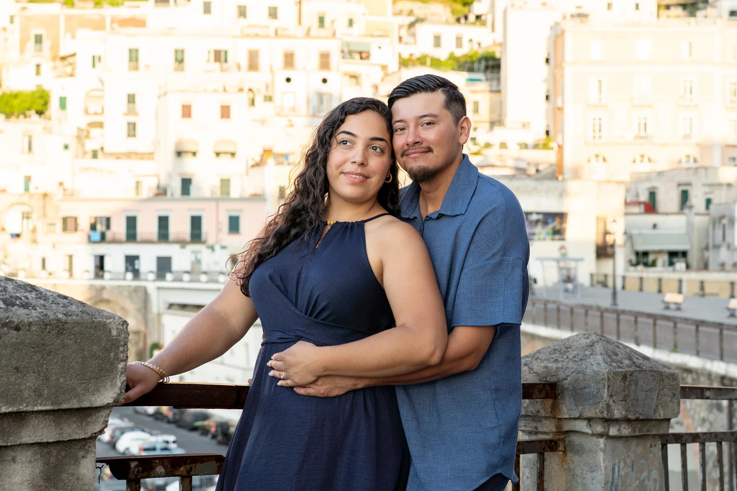 The couple smiling beside the balustrade in the sunlight