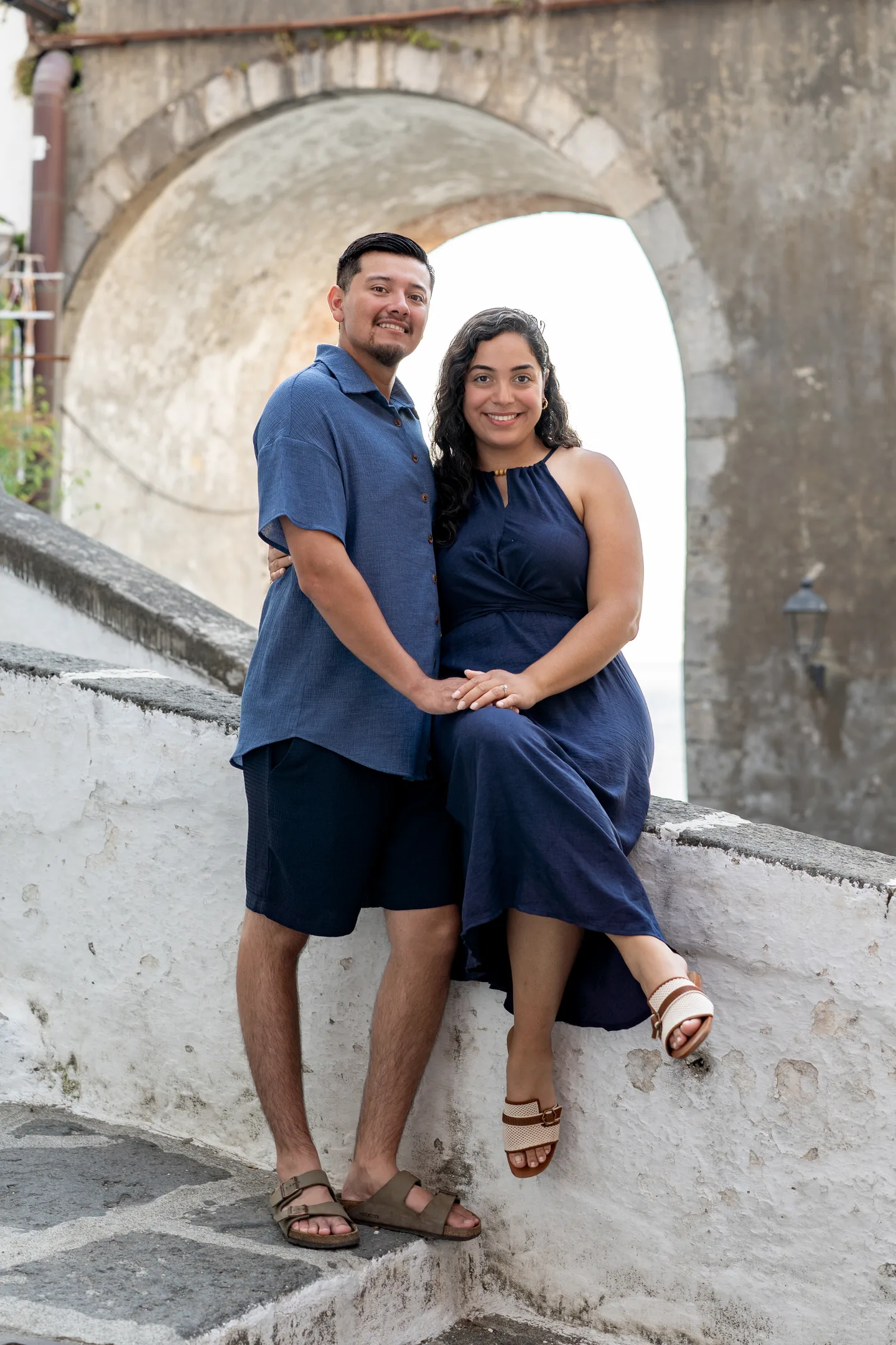The couple standing together beside the stone archway