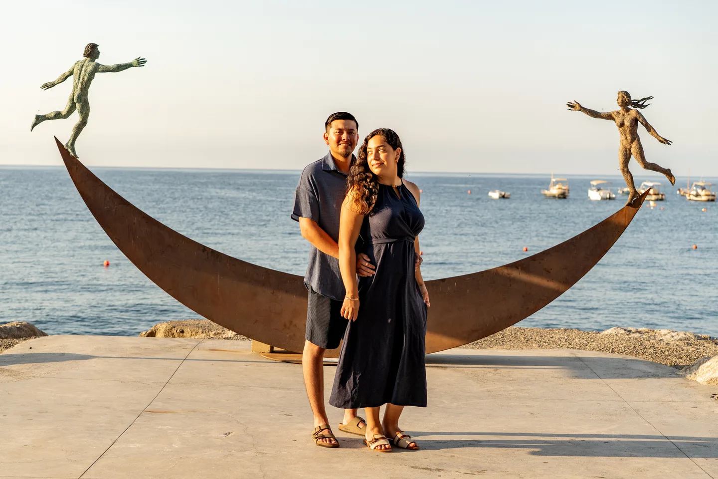 The couple embracing beside the sculpture and the sea