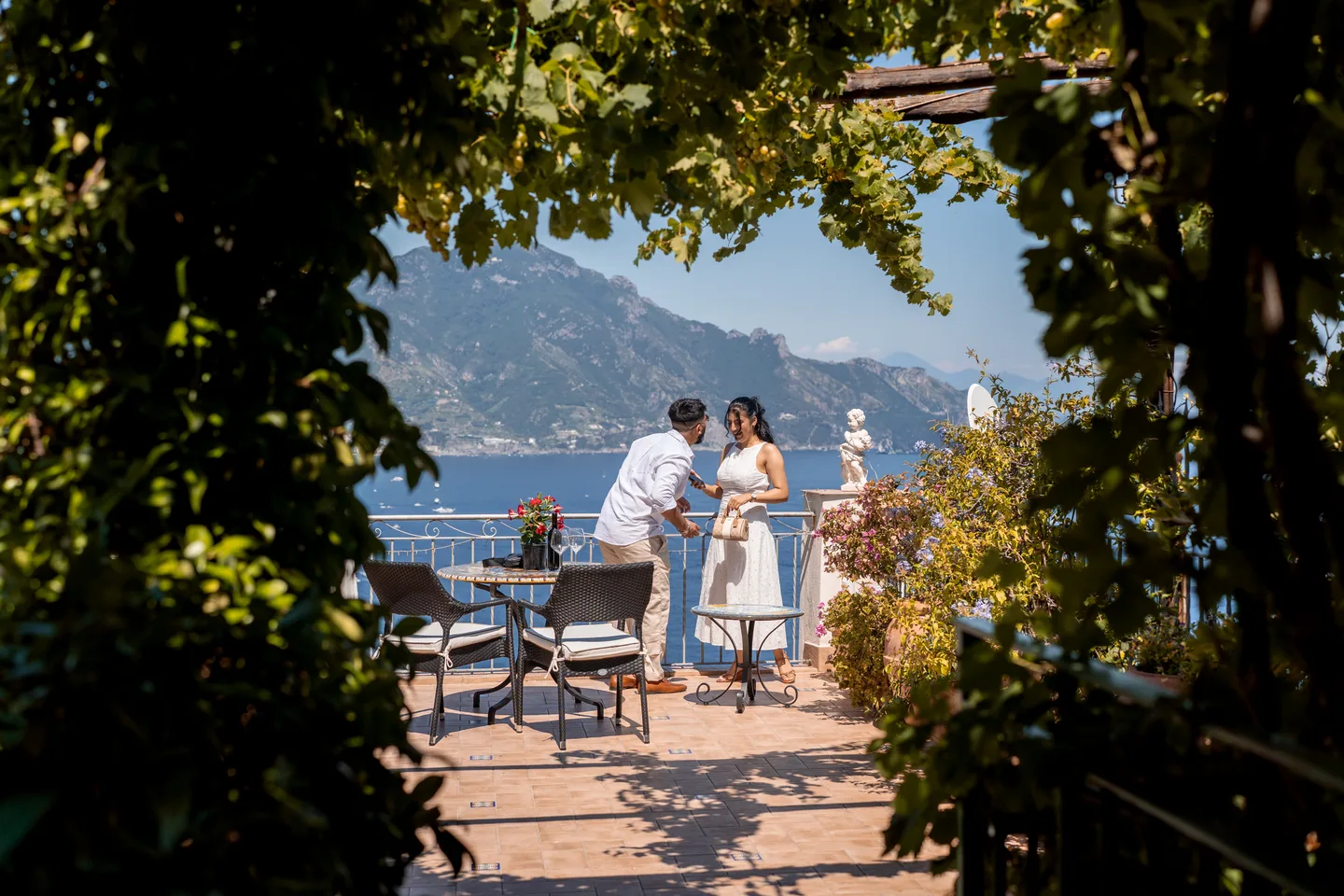 The couple on the villa terrace, framed by leaves