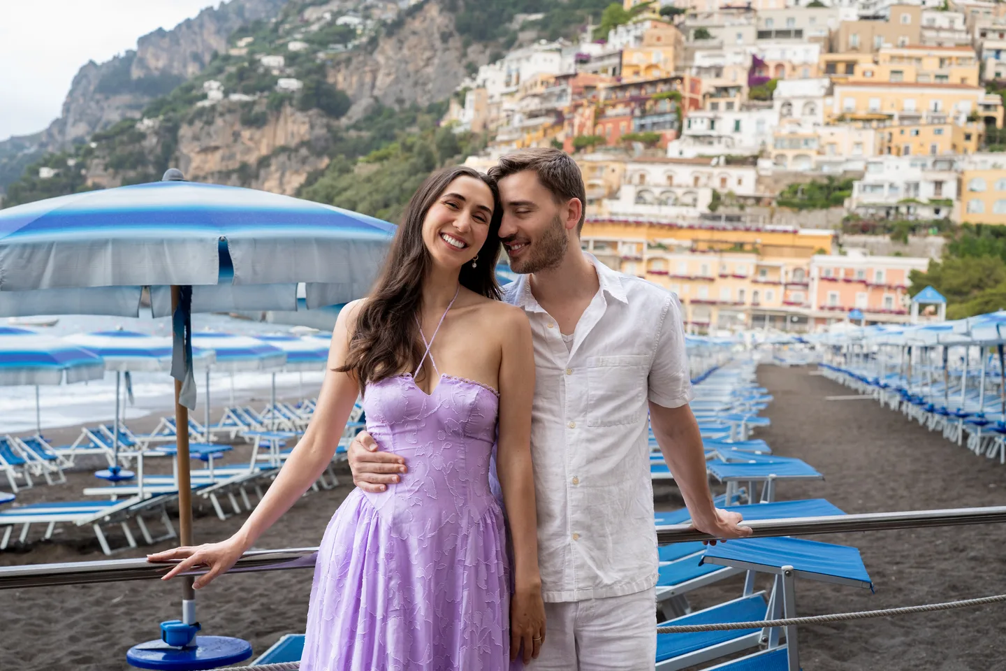 The couple leaning together by the blue beach chairs