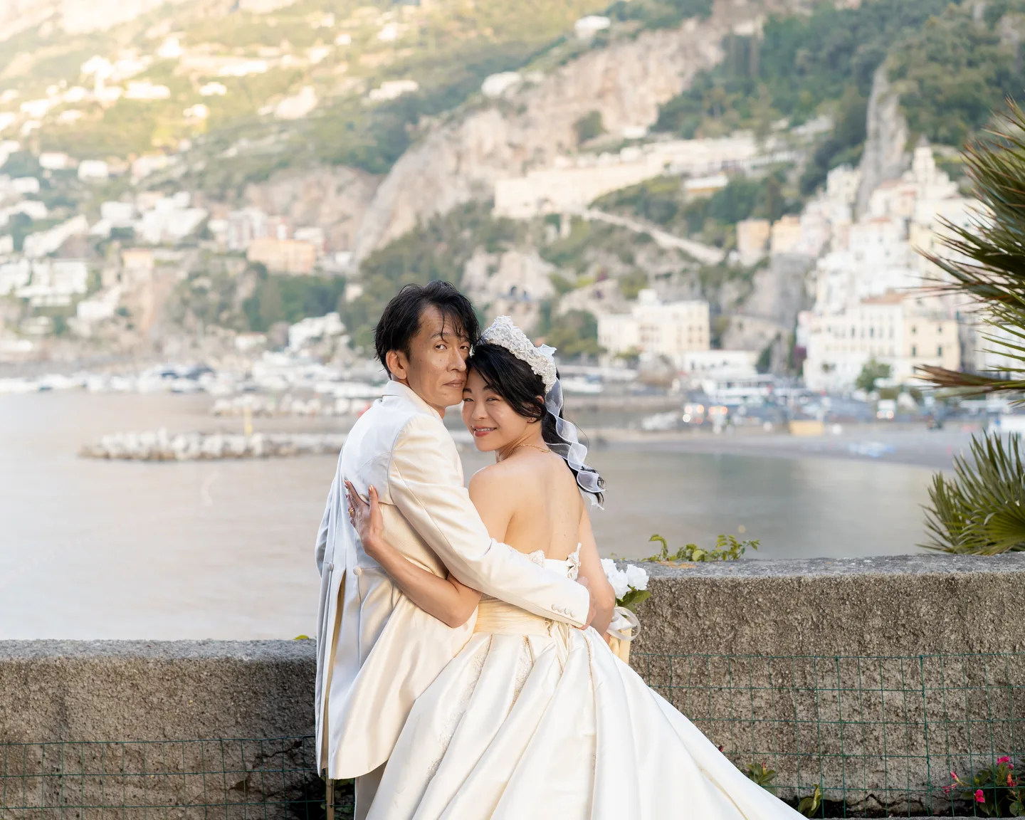 An embrace beside the sea wall with Amalfi behind them