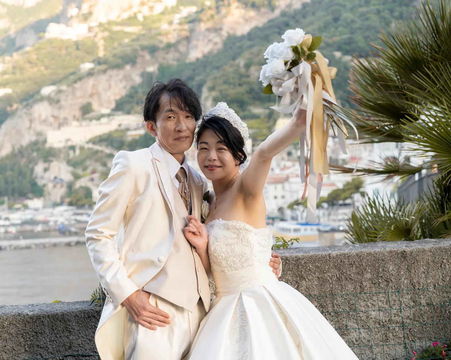The couple raising the bouquet in a playful waterfront portrait