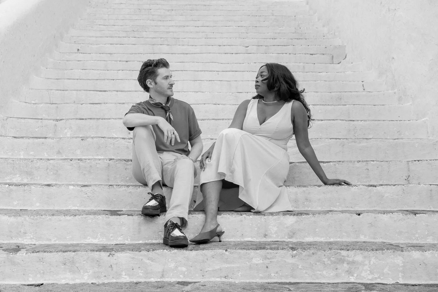 The couple seated together on the white staircase in black and white